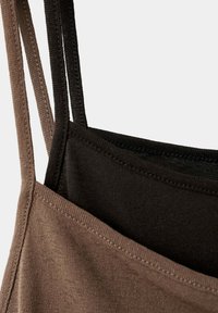 Gros plan sur des débardeurs en tissu marron et noir avec des bretelles fines, superposés sur un fond clair.