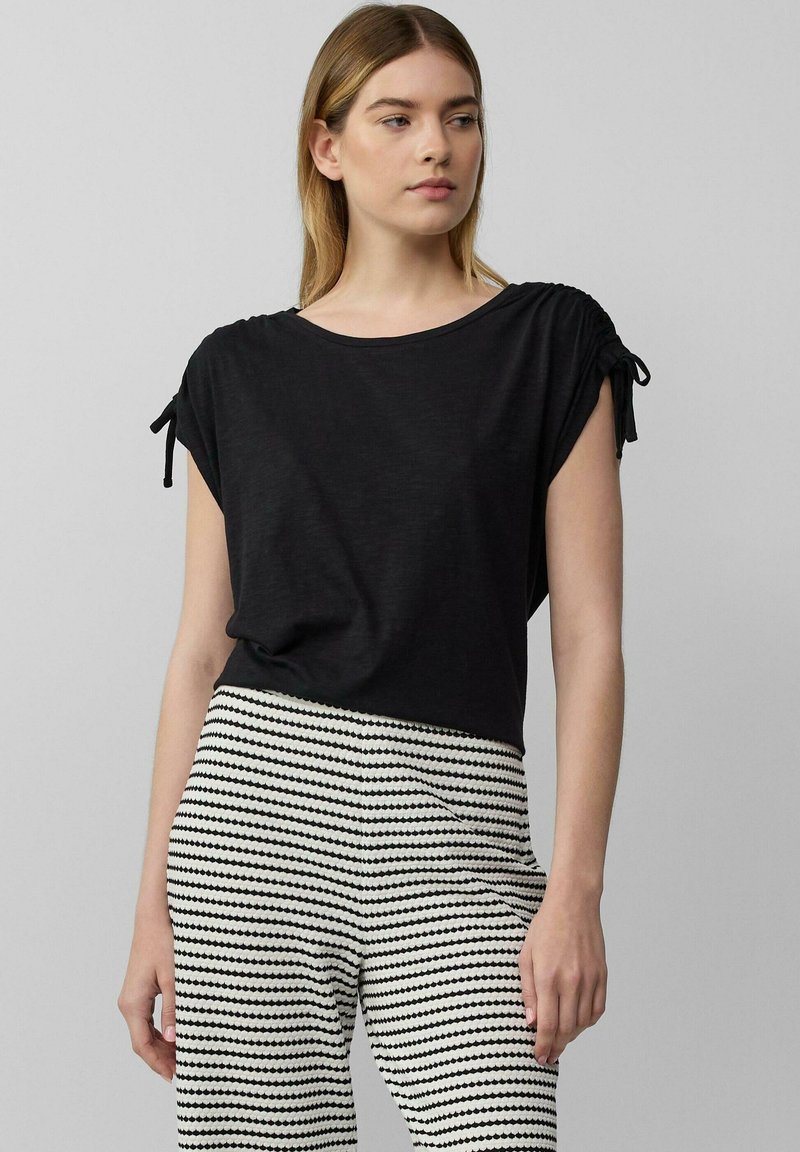 Zwarte top met korte mouwen en opgerolde mouwen, zachte textuur, gecombineerd met gepatterneerde zwart-witte gestreepte broek met afwisselende vormen.