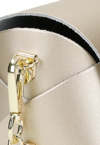 Metalická zlatá kabelka s hladkým povrchem. Má zaoblený klapku, vnitřní černou podšívku a zlaté zapínání s řetízkem.