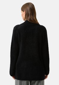 Černý kardigan s dlouhými rukávy vyrobený z měkkého, huňatého materiálu; má volný střih a jemný, texturovaný povrch. Jednoduchý design, bez dalších detailů.