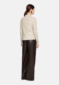 Beige Pullover mit hohem Kragen und gerippter Textur, kombiniert mit hochgeschnittenen, locker sitzenden schwarzen Lederhosen.