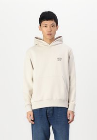 Lichtbeige hoodie van zacht materiaal, met een kangoeroezak, een capuchon met trekkoord en een klein logo op de borst gedrukt.
