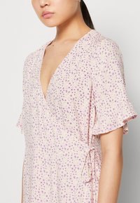 Light pink dress with short ruffled sleeves, featuring a floral pattern in purple and green. Wrap design with side tie detail.