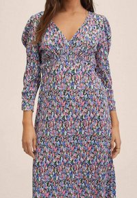 Robe maxi fleurie avec un décolleté en V, des manches longues, un corsage froncé et un motif multicolore de fleurs roses, bleues et vertes sur fond sombre.