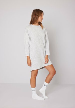 Lichtgrijze sweatshirtjurk met een relaxte pasvorm, lange mouwen en ronde halslijn. Gepaarde met witte sokken met zwarte tekst.