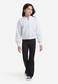 Šedá mikina na zips so hladkou textúrou, klokanie vrecká a priliehavý pás, kombinovaná s čiernymi rozšírenými nohavicami a čiernymi teniskami.