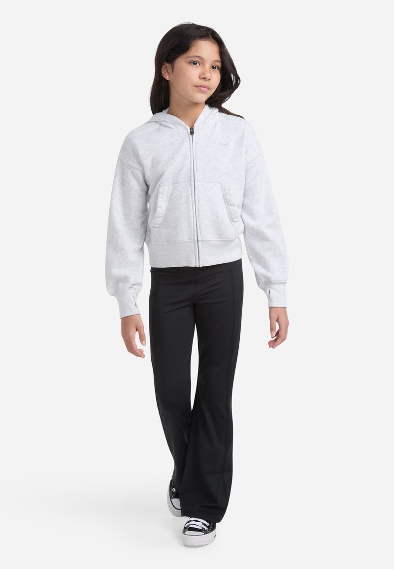 Šedá mikina na zips so hladkou textúrou, klokanie vrecká a priliehavý pás, kombinovaná s čiernymi rozšírenými nohavicami a čiernymi teniskami.