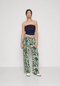 Meresinine rihmadeta top koos rohelise ja kreemika lehemustriga laiade pükstega. Model kannab valgeid kontsaga saapaid ja pärliketti.