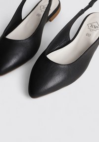 Bailarinas negras de tiras traseras con punta afilada, hechas de cuero suave. Tienen un tacón bajo y un diseño recortado en los laterales.