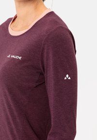 Camicia a maniche lunghe in tessuto viola scuro con scollatura rosa chiaro, caratterizzata da un logo bianco sul petto e un piccolo logo sulla manica.
