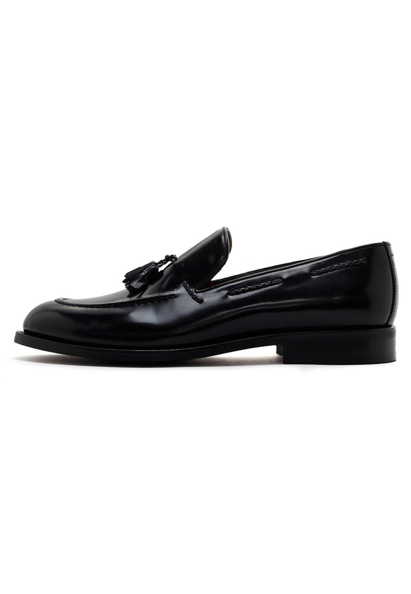 Mocassin en cuir noir avec des glands, bout rond, couture contrastante et un talon de hauteur moyenne. Texture lisse et finition polie.