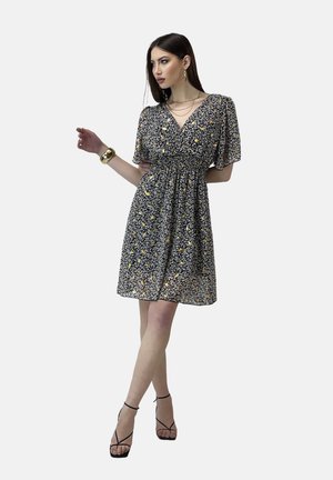 Bloemige jurk met korte mouwen en een V-hals, zwarte basis, gele en witte patronen, geplooide taille, knie-lengte, gedragen met strappy hakken.