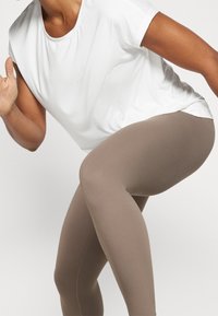 Camiseta deportiva blanca de manga corta combinada con leggings marrón claro, que destaca una textura lisa y ajustada adecuada para ropa activa.