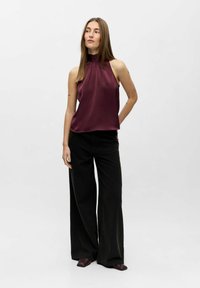 Burgundy satin halterneck-top med draperad halsringning, kombinerad med högmidjade svarta vida byxor och mörkbruna fyrkantiga skor.