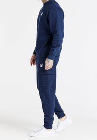 Granatowa bluza dresowa i pasujące dresy wykonane z miękkiego materiału; bluza ma okrągły dekolt i haftowane logo; dresy mają boczne kieszenie.