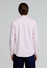 Camisetă cu dungi roz deschis, cu guler și manșete butonate, cu mâneci lungi, textură moale, margine curbă, purtată peste blugi închisi.
