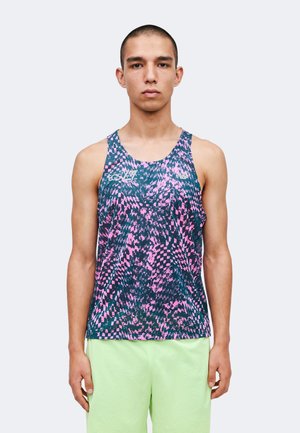 Jeune homme aux cheveux courts portant un débardeur de sport sans manches avec des motifs abstraits rose et bleu foncé ainsi qu’un short vert clair.