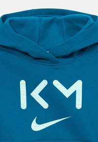 Felpa con cappuccio color teal con lettere "KM" azzurre e logo swoosh Nike sul petto, che mostra dettagliati punti di cucitura sul cappuccio.