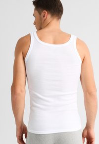 White ribbed tank top with a round neckline and wide shoulder straps, fitted design, and smooth texture. Shown from the back.