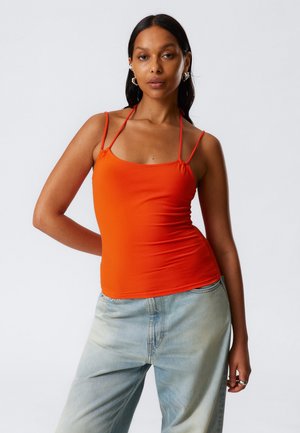 Orange sleeveless top with thin adjustable straps, fitted design, and smooth texture, paired with light blue denim jeans.