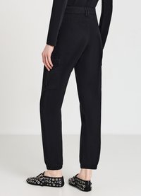 Schwarze Cargo-Shorts mit lockerer Passform, elastischen Bündchen, seitlichen Taschen und glattem Textil. Getragen mit verzierten schwarzen Slippers.