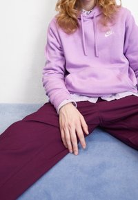 Ljuslila Nike-hoodie med känguruficka, matchad med djup burgundy byxor. En texturerad, lager-på-lager skjorta syns under hoodien.