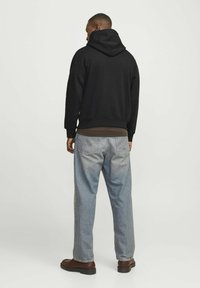 Sudadera de algodón negra con capucha, corte relajado, combinada con jeans de mezclilla azul claro y botas marrones. Diseño simple sin logotipos ni acentos visibles.