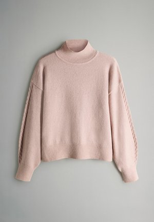 Gaiši rozā adīts pusaudžu džemperis ar augstu ribotu apkakli, nolaistām pleciem un raksturīgu paneļu detaļām uz piedurknēm.