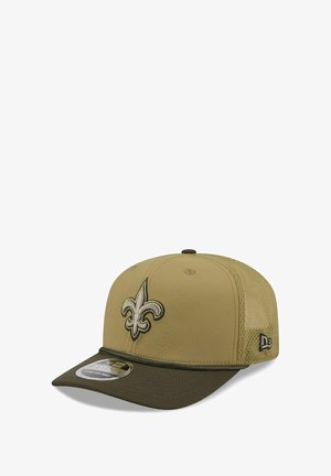 Casquette beige avec des panneaux latéraux en filet. Présente un logo en 3D brodé de fleur de lys et une visière plate avec une bordure contrastante en vert foncé.