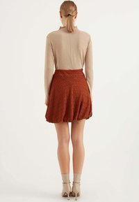 Ljusbeige långärmad topp i kombination med en mönstrad orange zigzag-uppskuren kjol och beige ankelstövlar sedd från en bakvinkel.