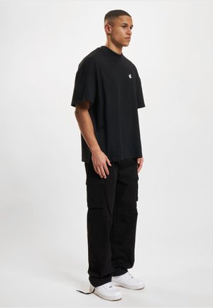 Musta ylisuurennettu t-paita pyöreällä kaula-aukolla ja pienellä logolla. Yhdistetty mustiin cargo-housuihin ja valkoisiin tennareihin, joissa on reikätyödetaljit.