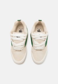 Beige canvas sneakers with green side accents, white laces, and textured soles. Rounded toe design and branded inner lining.