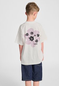 Vit kortärmad T-shirt med en stor rosa blommig grafik med svarta detaljer på baksidan, tillsammans med mörka denimshorts.