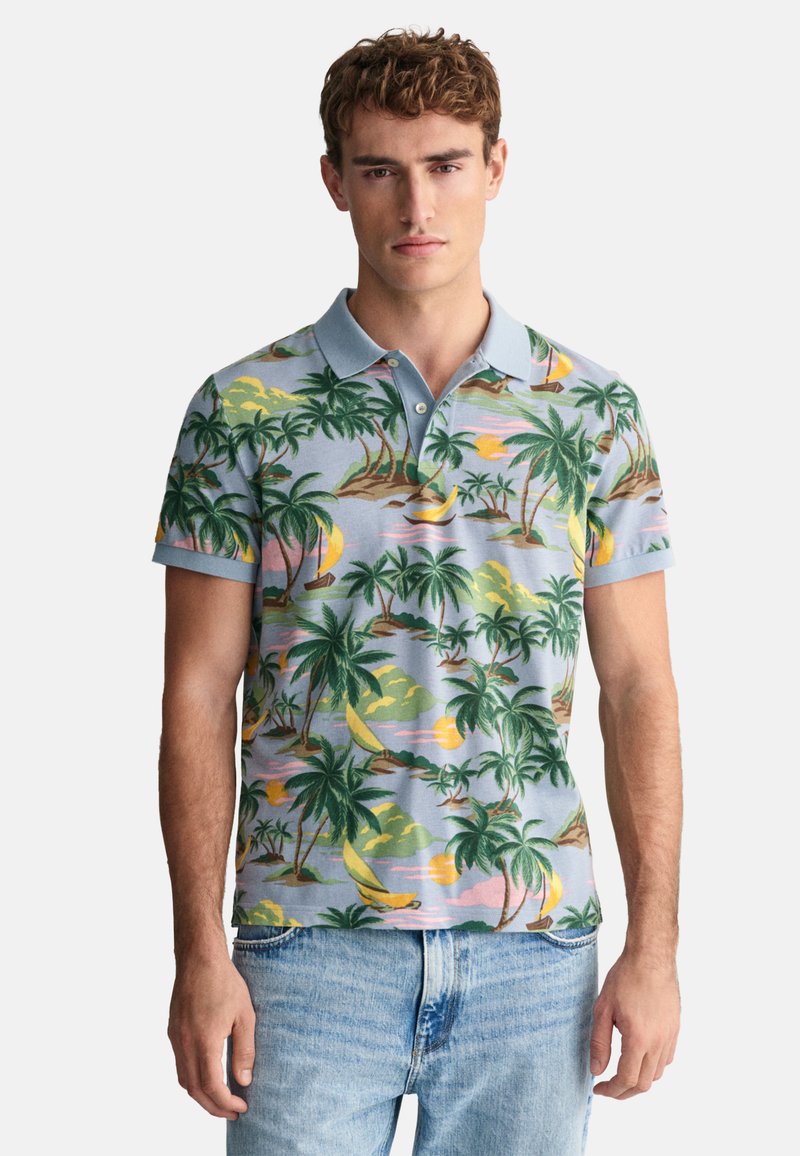 Polo tričko s modrým pozadím a vzory tropických palm a západu slunce. Krátké rukávy, límec a měkký bavlněný materiál.