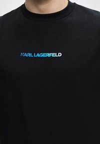 Μαύρο μπλουζάκι με στρογγυλή λαιμόκοψη με αποτύπωση "KARL LAGERFELD" με μπλε και λευκά γράμματα στο στήθος.