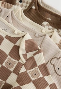Soft ribbed baby bodysuits in beige and brown tones, featuring checkered and bear face patterns, layered and folded closely together.