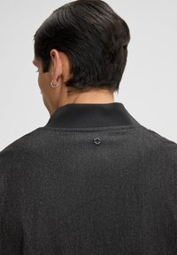 Giacca nera con texture, dotata di colletto, un motivo sottile e un piccolo emblema nero sul retro vicino al collo.
