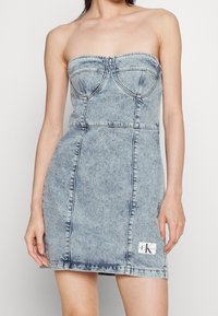 Jeansvänster klänning utan axelband i ljusblått, med en figurnära bodice, subtila sömnadsdetaljer och en logotypapplikation nära fållan. Slät textur.