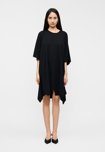 Μαύρο oversized φόρεμα σε στυλ t-shirt με στρογγυλεμένο λαιμό, κοντά μανίκια και ασύμμετρο τελείωμα. Κατασκευασμένο από απαλό, λείο ύφασμα.