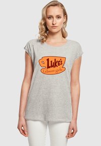 Šedé tričko vyrobené z měkké tkaniny, s velkým oranžovým designem a textem "Luke's" a "Gilmore girls". Krátké rukávy a volný střih.