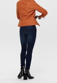 Pomarańczowa zamszowa kurtka, dopasowane ciemnoniebieskie dżinsy, czarne botki z grubymi obcasami. Kurtka ma szczegółowe przeszycia, a dżinsy posiadają tylne kieszenie.