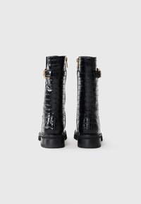 Botas de tobillo de cuero negro con textura de cocodrilo, con hebillas doradas y cremalleras, y una resistente suela de goma negra.