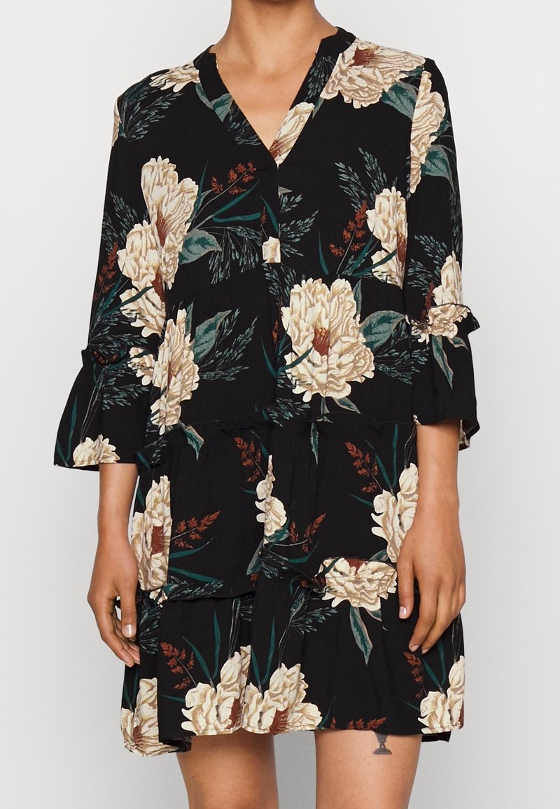 Svart blommig klänning med stora beige blommor och gröna blad, långa ärmar med volanger och en avslappnad passform med en knytning vid midjan.