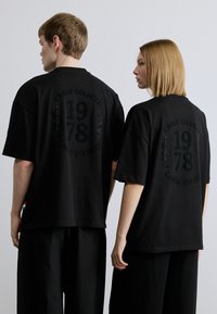 Μαύρα υπερμεγέθη T-shirts με υφασμάτινο γραφικό σχέδιο, που απεικονίζουν "CARLO COLUCCI" και "1978" με σκοτεινά γράμματα στην πλάτη.