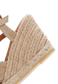 Beige wedge sandaal van geweven jute materiaal, met een gestructureerd oppervlak en een leren bruine band. Accenten zijn onder andere een pareldetails langs de band.