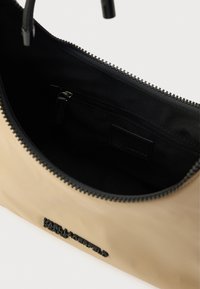 Bézs cipzáras táska fekete béléssel, textil külsővel és fekete logórészlettel. A belsejében cipzáras zseb található.