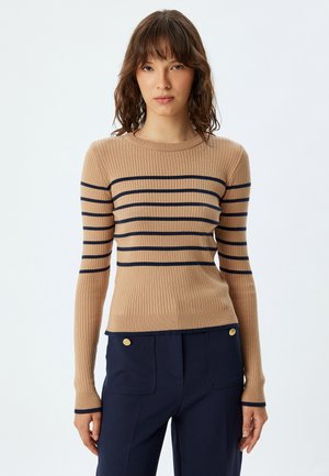 Geribbelde, beige lange mouwen top met horizontale marineblauwe strepen. Ronde halslijn, slim fit ontwerp, gecombineerd met high-waisted marineblauwe broek met gouden knopen.