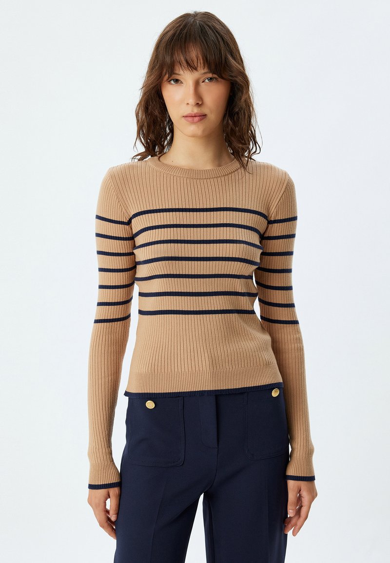 Maglia a maniche lunghe beige a coste con righe orizzontali blu navy. Collo rotondo, design aderente, abbinata a pantaloni blu navy a vita alta con bottoni dorati.