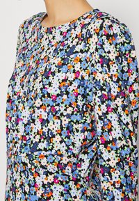 Bluzka w kwiatowy wzór z lekkiego materiału, z niebieskimi, różowymi i zielonymi akcentami na czarnym tle; okrągły dekolt i krótkie rękawy.