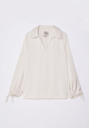 Blouse longue beige clair à manches longues avec un col, une ouverture en V et des poignets froncés avec des liens. Texture douce avec un motif minimal.